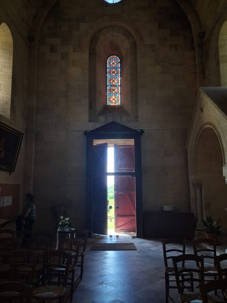 Intérieur de l'église en pénombre, porte ouverte sur la lumière et vitrail